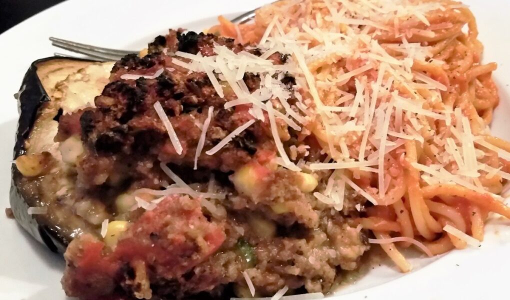 Serving of stuffed egg[lant alongside serving of spaghetti noodles with shredded parmesan cheese.