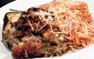 Serving of stuffed egg[lant alongside serving of spaghetti noodles with shredded parmesan cheese.