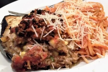Serving of stuffed egg[lant alongside serving of spaghetti noodles with shredded parmesan cheese.