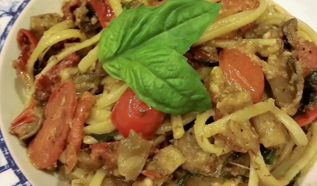 Extreme close-up of a single serving of spaghetti noodles and eggplant ragout in white bowls on wooden tabletop