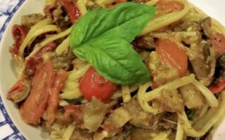 Extreme close-up of a single serving of spaghetti noodles and eggplant ragout in white bowls on wooden tabletop