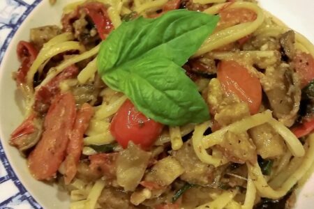 Extreme close-up of a single serving of spaghetti noodles and eggplant ragout in white bowls on wooden tabletop