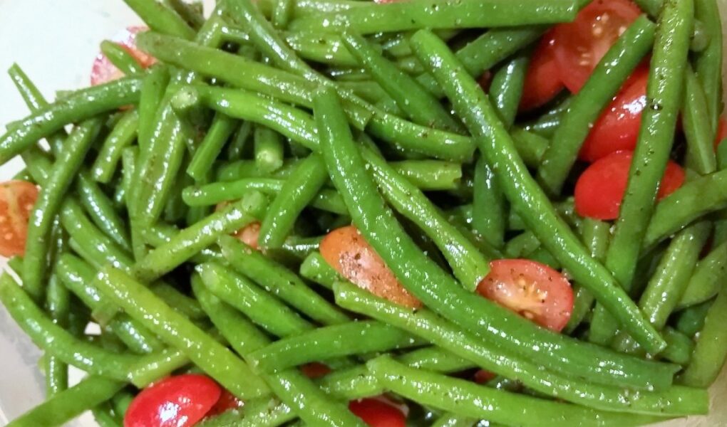 Close-up of blanched green beans and tomatoes dressed in oil and seasonings.