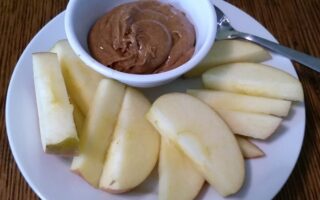 Bowl of spiced almond butter served with apple slices on a dessert plate