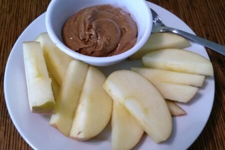 Bowl of spiced almond butter served with apple slices on a dessert plate