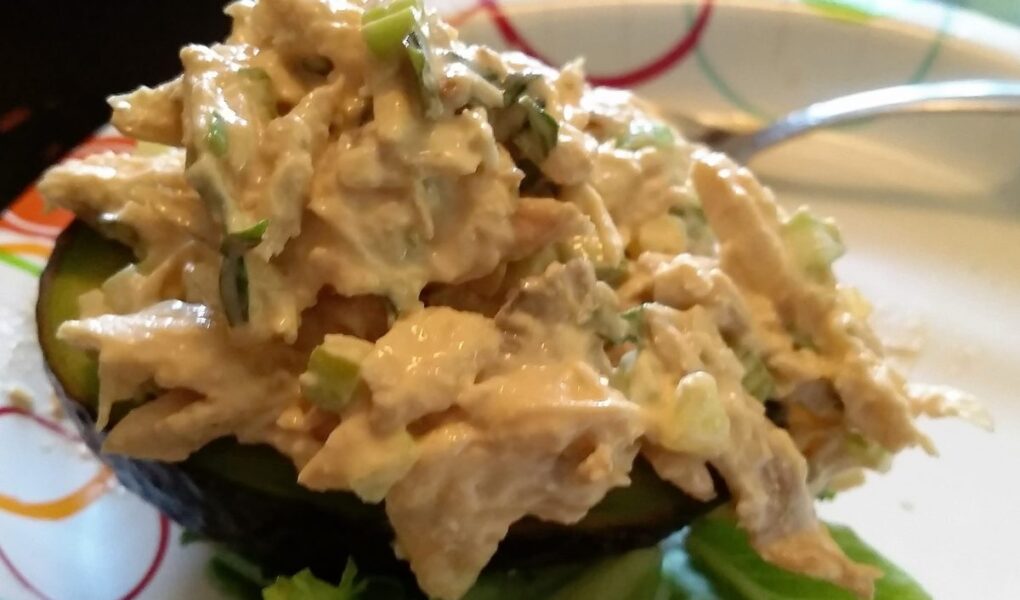 Finished chicken salad served on half an avocado on paper plate