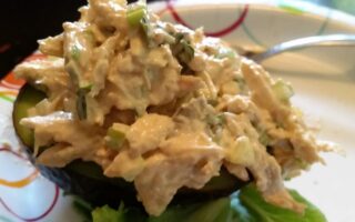 Finished chicken salad served on half an avocado on paper plate