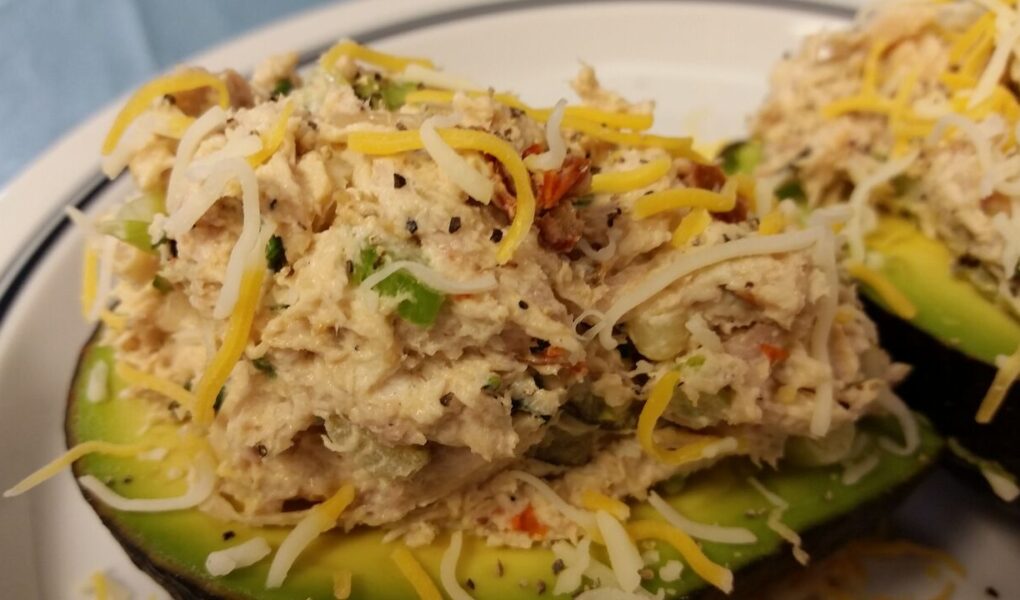 Close-up of finished cheicken salad served on two avocado halves and topped with additional shredded cheese served on a white plate
