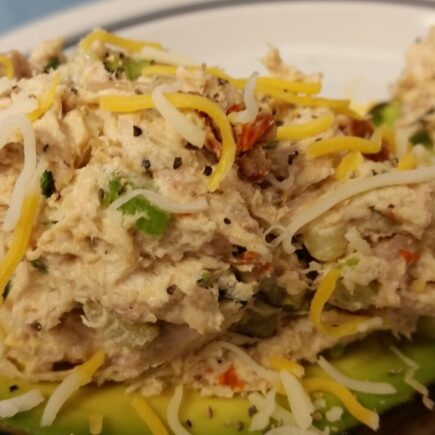 Close-up of finished cheicken salad served on two avocado halves and topped with additional shredded cheese served on a white plate
