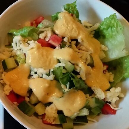 Finish vinaigrette poured over tossed salad in white bowl