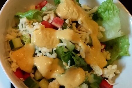 Finish vinaigrette poured over tossed salad in white bowl