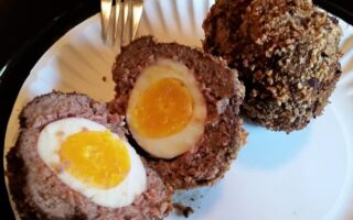 Two scotch eggs served on white paper plate, one cut in half