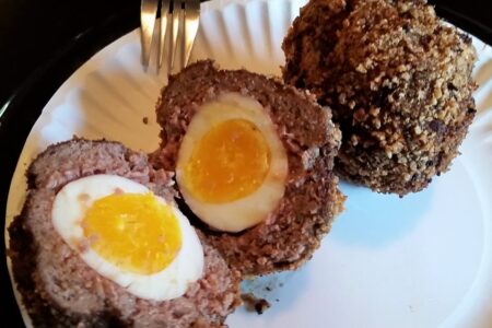 Two scotch eggs served on white paper plate, one cut in half