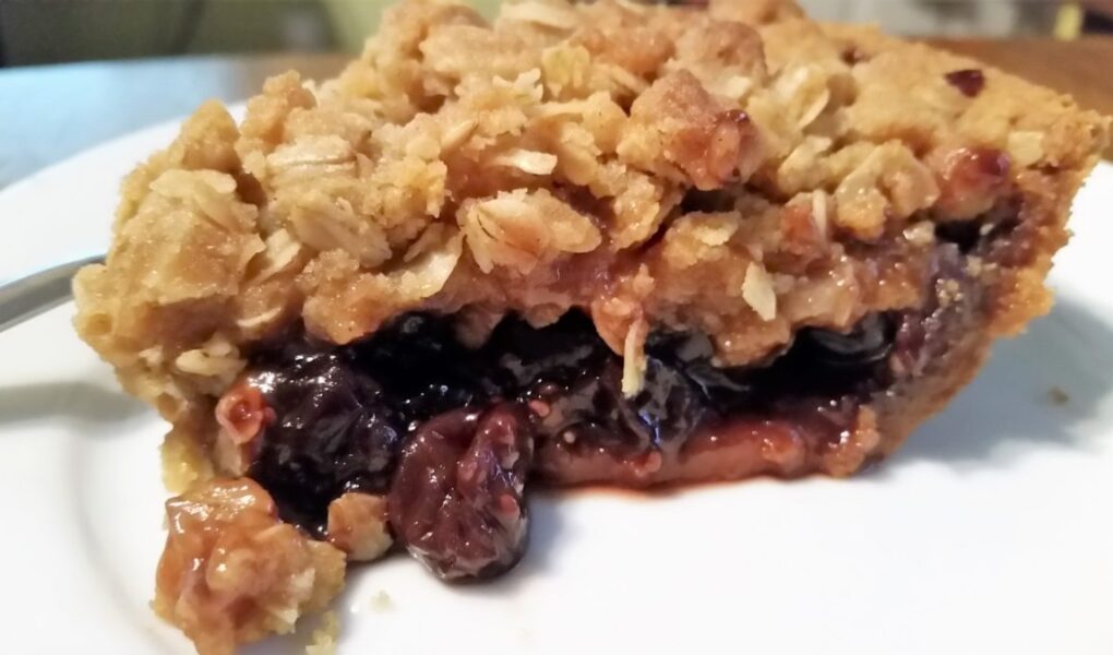 Side view of jam crumble pie on a white dessert plate
