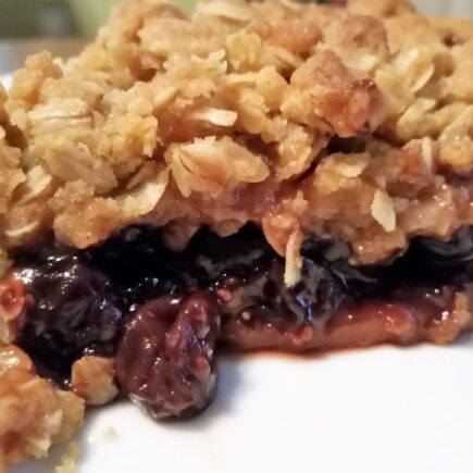 Side view of jam crumble pie on a white dessert plate