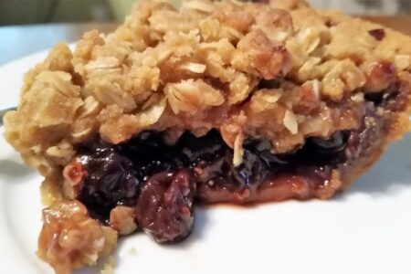 Side view of jam crumble pie on a white dessert plate