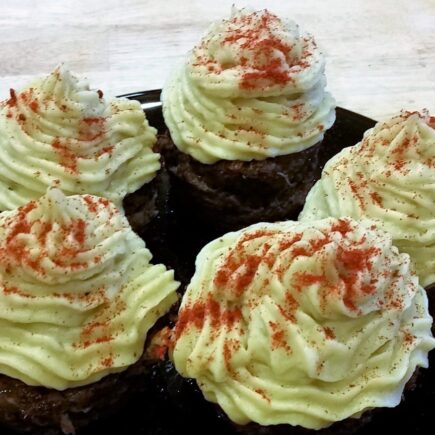 Close-up of black serving plate with five finished liver cupcakes topped with decorative mashed yams and sprinkled with paprika
