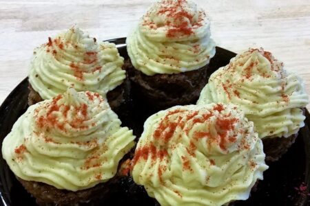 Close-up of black serving plate with five finished liver cupcakes topped with decorative mashed yams and sprinkled with paprika