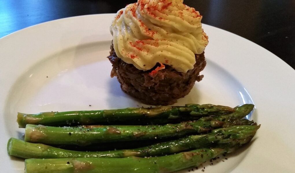Another view of Individual liver cupcake with mashed yam topping served alongside roasted aspragus on a white diner plate