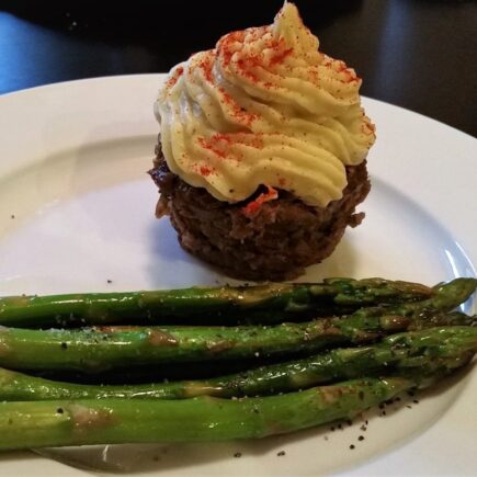 Another view of Individual liver cupcake with mashed yam topping served alongside roasted aspragus on a white diner plate