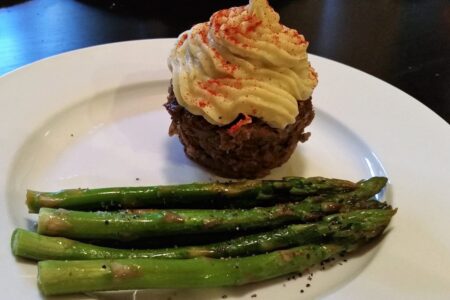 Another view of Individual liver cupcake with mashed yam topping served alongside roasted aspragus on a white diner plate