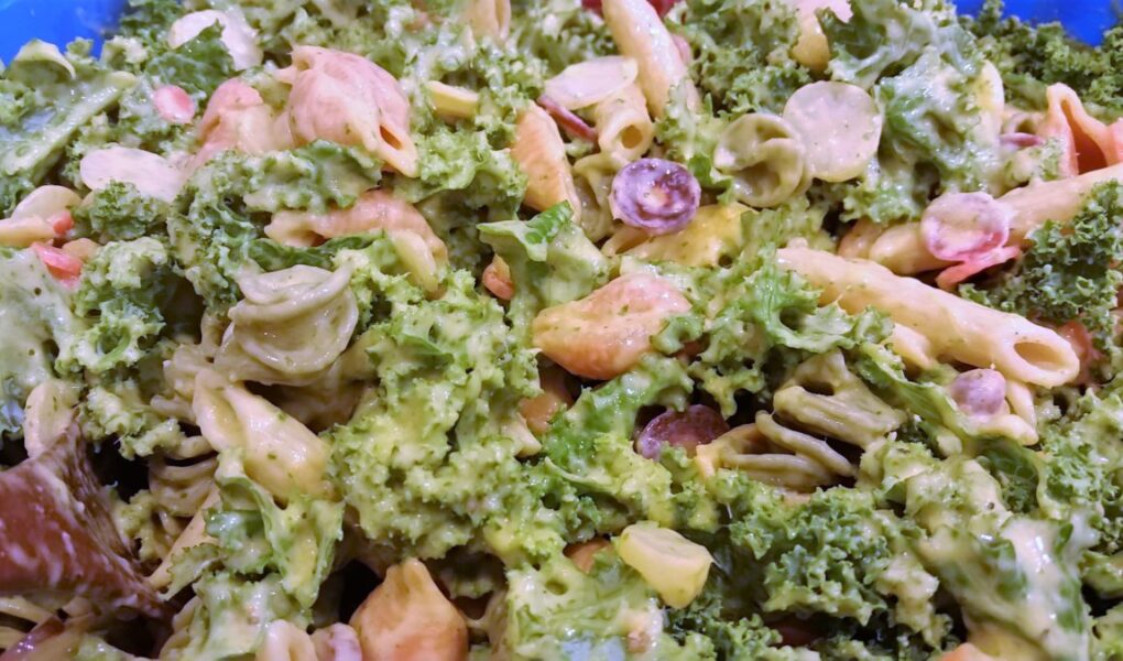 Close up of salad showing kale, dressing along with penne and spiral pasta and grapes