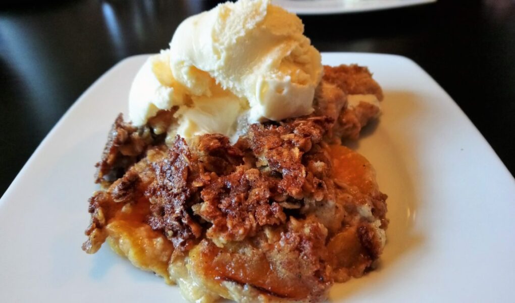 Peaches and Cream Cobbler on plate, topped with scoop of vanilla ice cream