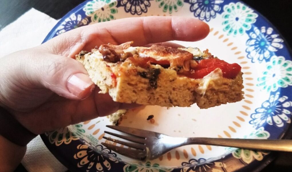 YiaYia's hand holding piece of chick crusted pizza viewed from the edge to show texture.