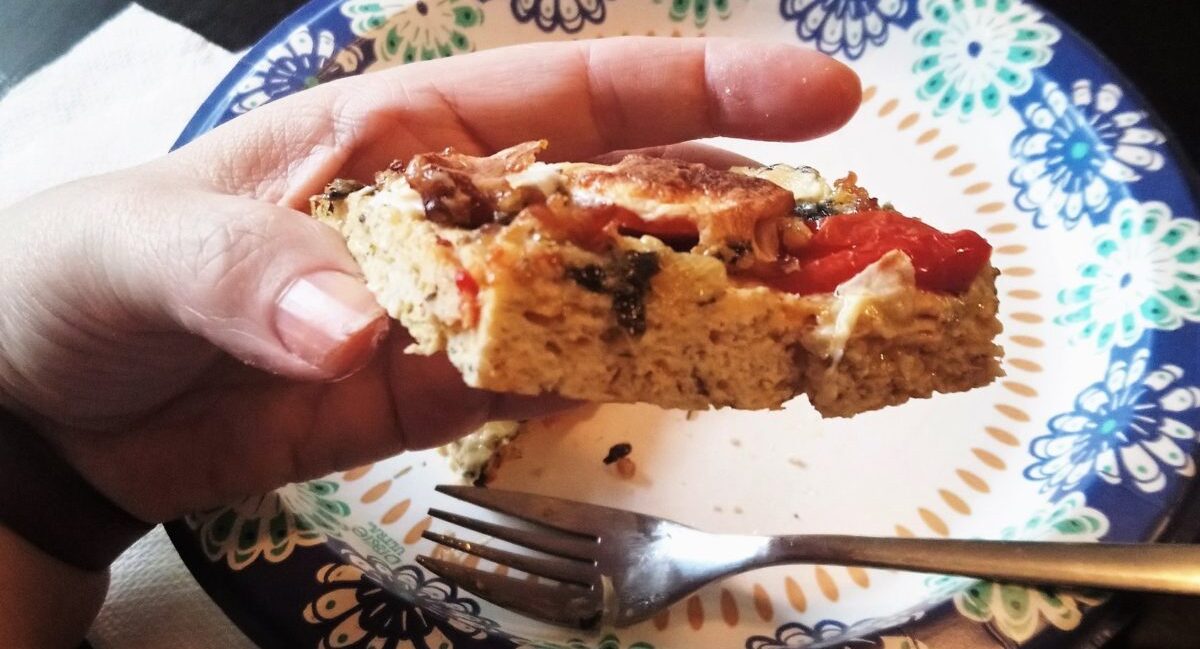 YiaYia's hand holding piece of chick crusted pizza viewed from the edge to show texture.