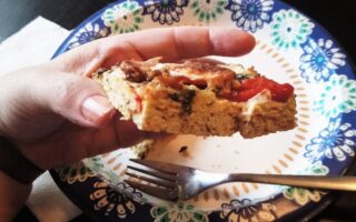 YiaYia's hand holding piece of chick crusted pizza viewed from the edge to show texture.