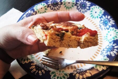 YiaYia's hand holding piece of chick crusted pizza viewed from the edge to show texture.